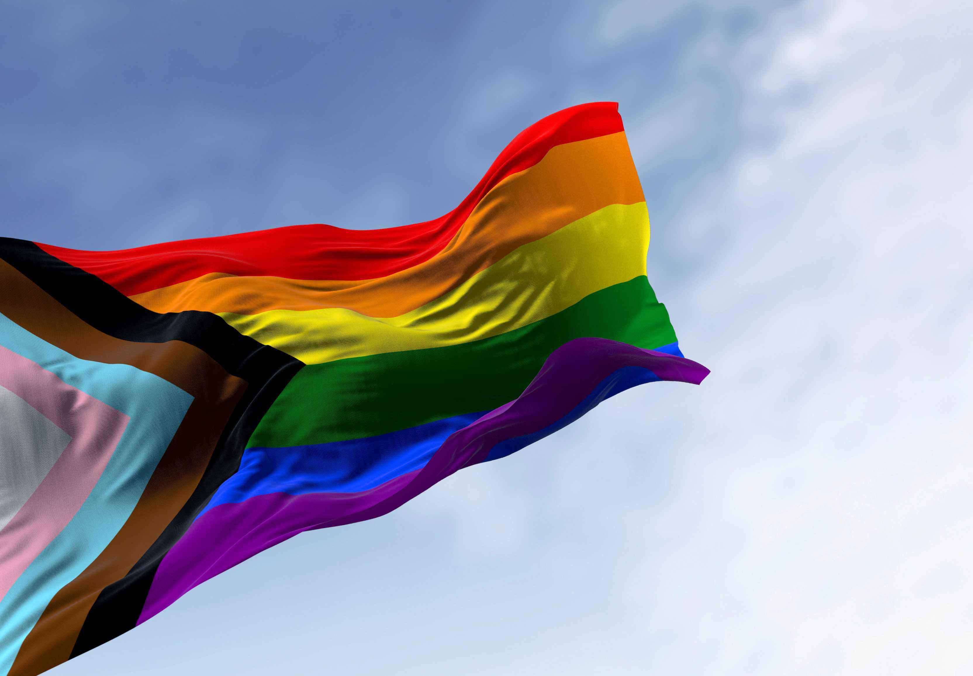 Progress rainbow flag against blue sky
